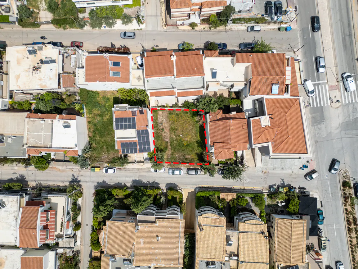 Aerial view of a vacant lot outlined in red, surrounded by houses with orange tile roofs and a street with parked cars.