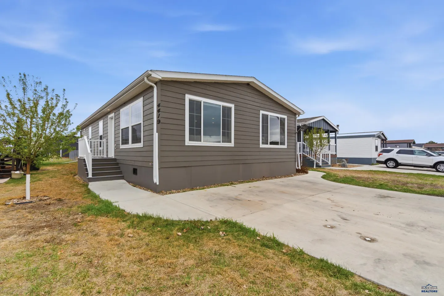 Exterior view of a gray single-story home with white trim, a concrete driveway, and a small front yard.