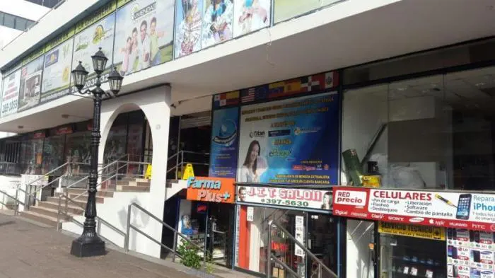 A street-level view of a commercial building with various storefronts, including a pharmacy and a salon. A black lamppost stands in front of the building.