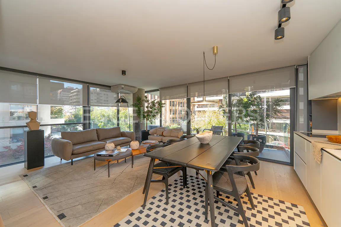 Bright living room with a gray sofa, black dining table and chairs, and large windows with city views.