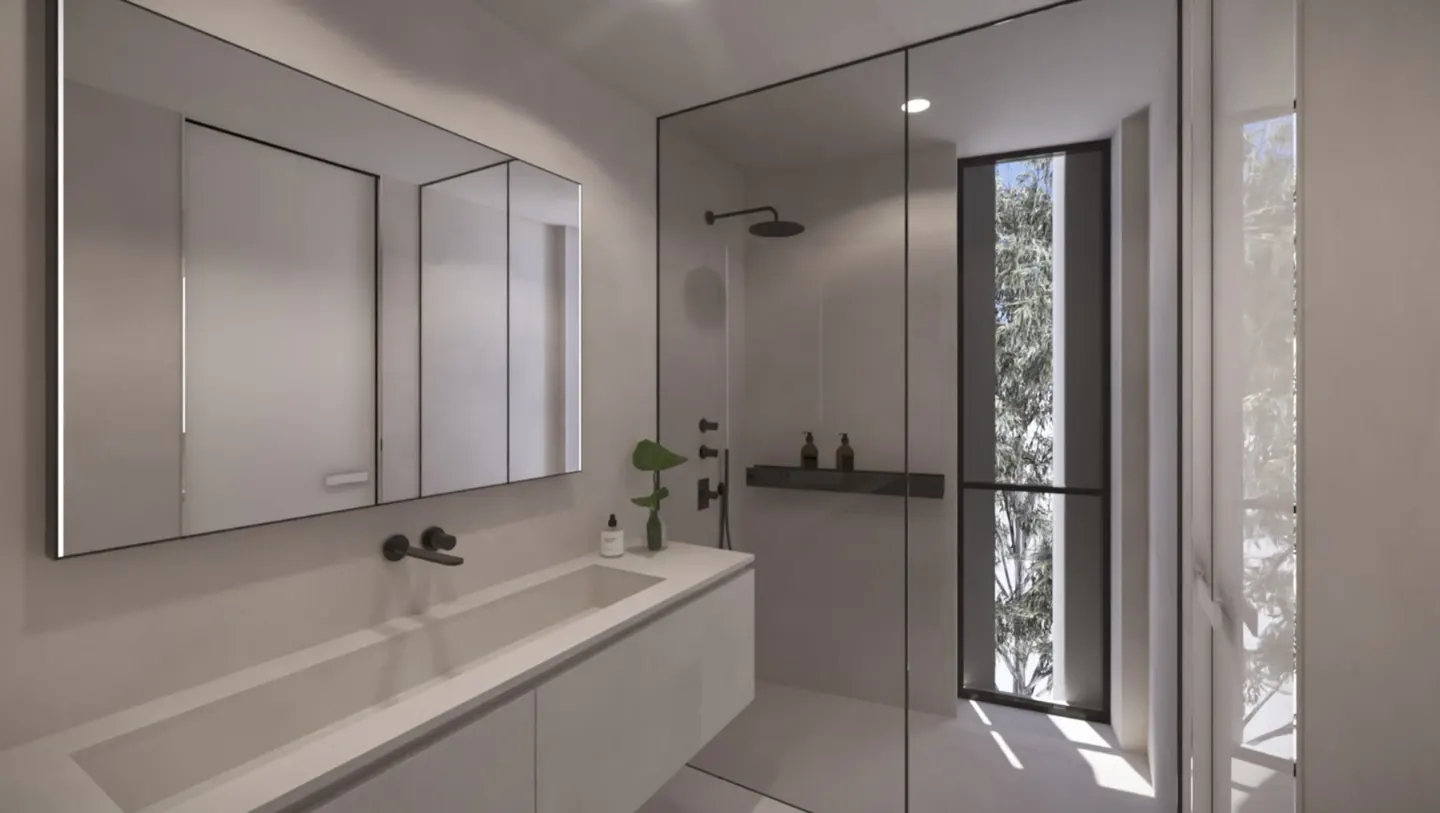 Modern bathroom with a long white sink, black faucet, and a large mirror. A glass-enclosed shower is visible with a black frame and a view of trees outside.