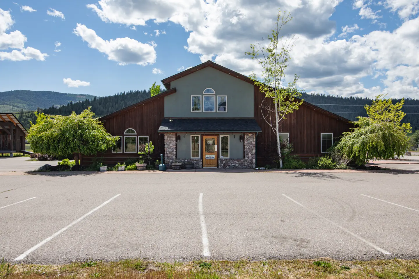 Exterior of a two-story building with brown wood siding and a green facade, stone pillars, and a parking lot.