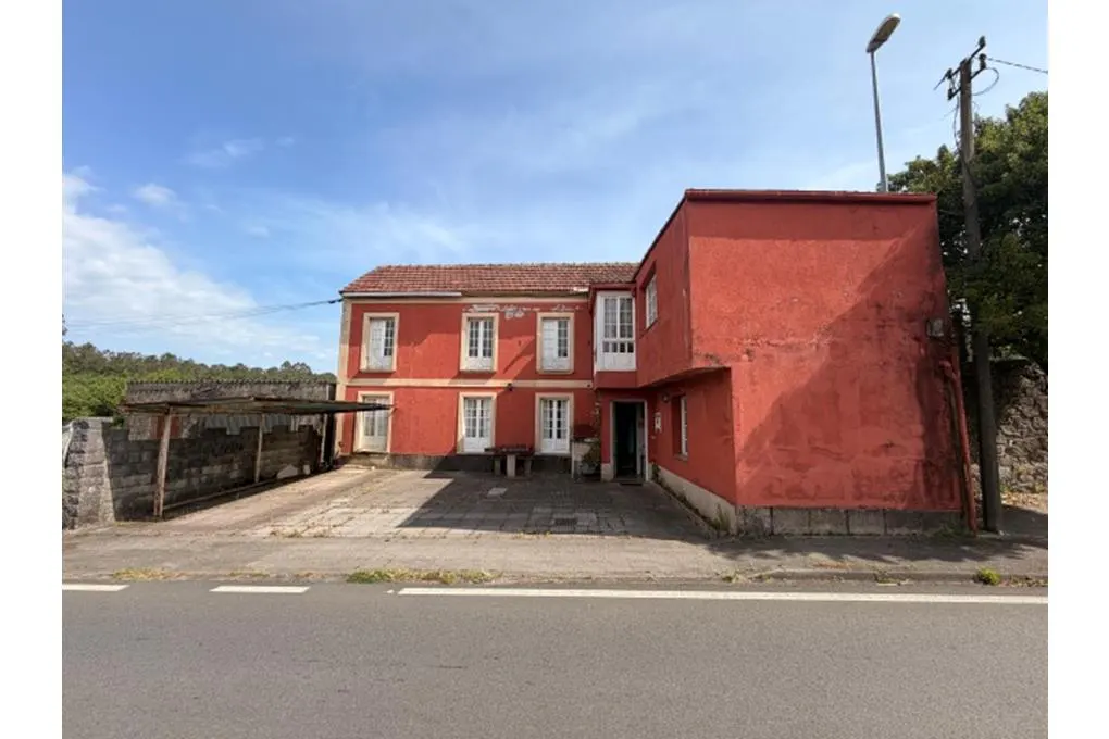 Two-story red house with white windows and a red tile roof, viewed from the street on a sunny day.
