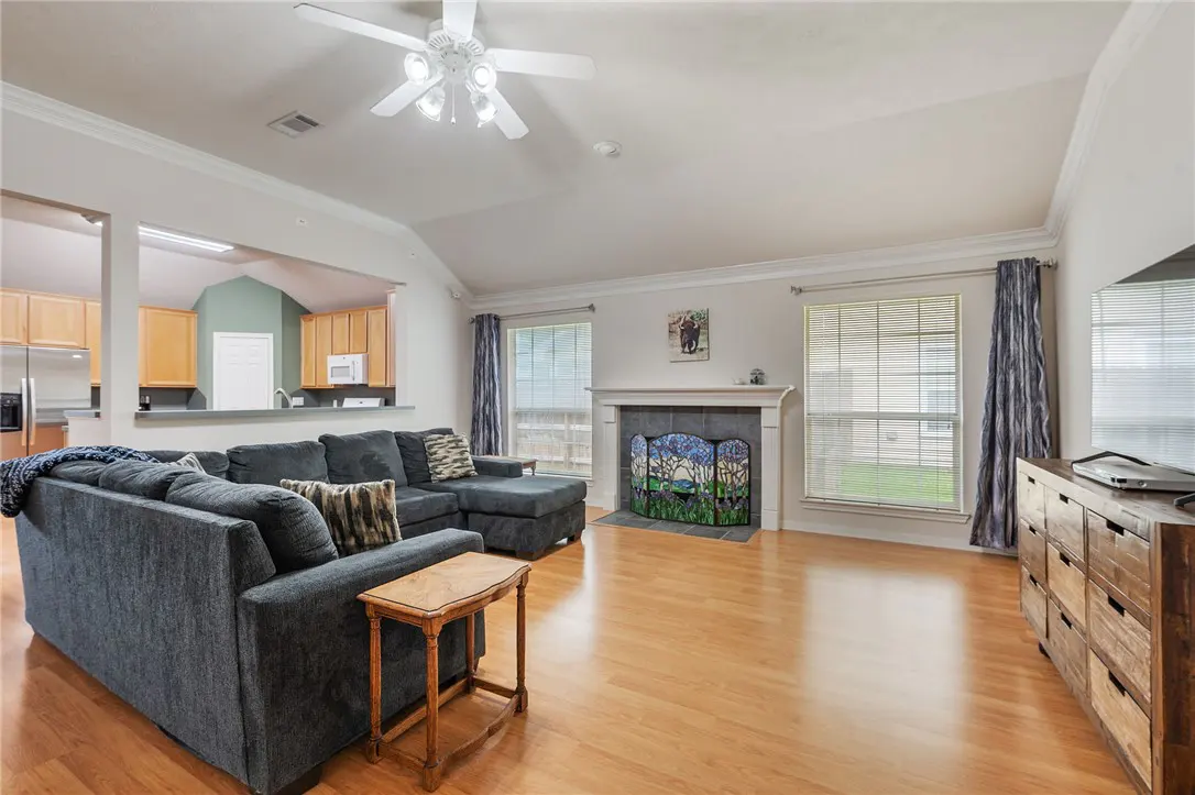 Living room with hardwood floors, a gray sectional sofa, and a fireplace with a decorative screen. A kitchen is visible through an opening.