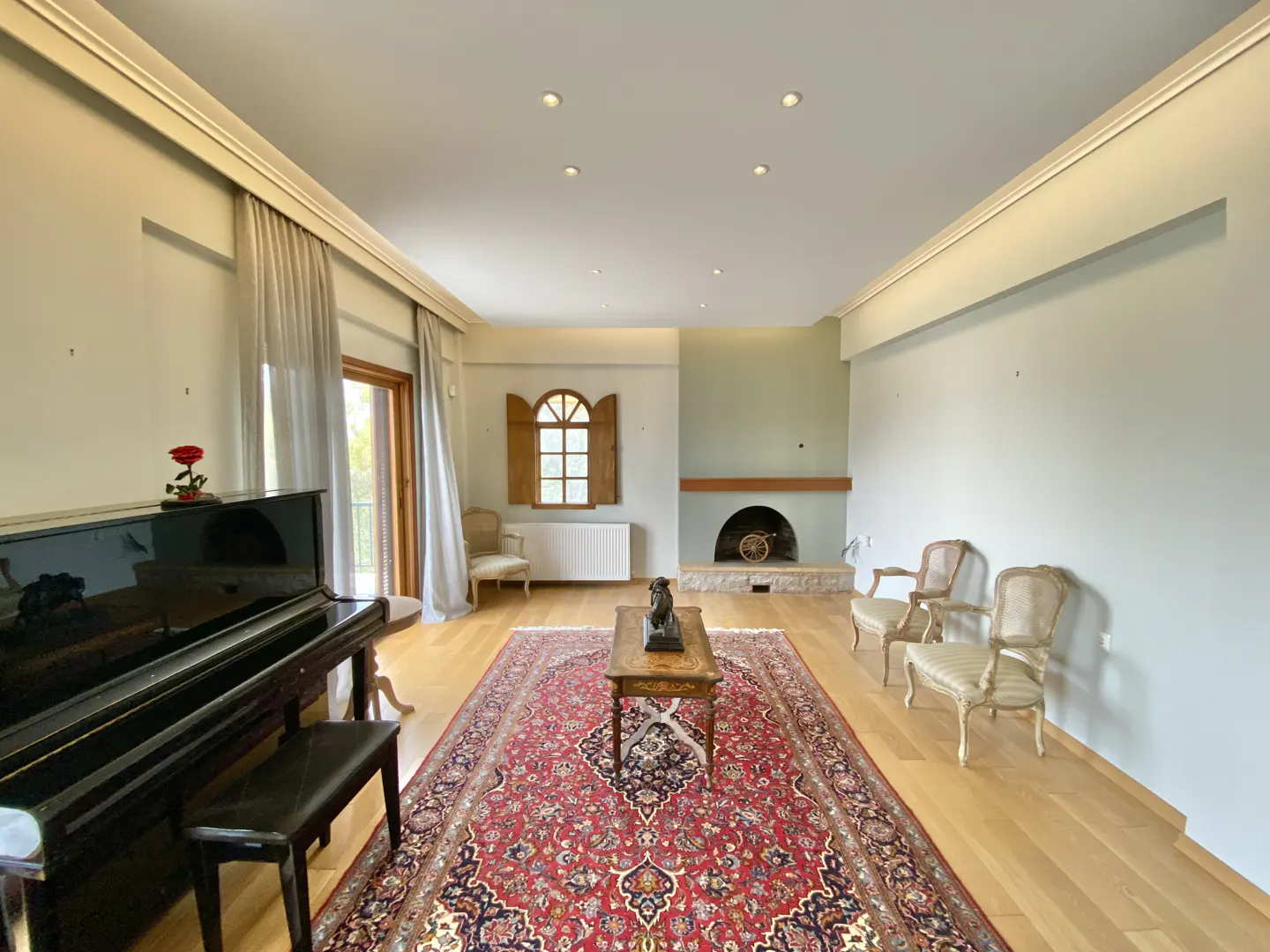 A spacious living room with a piano, fireplace, and red rug on a light wood floor.