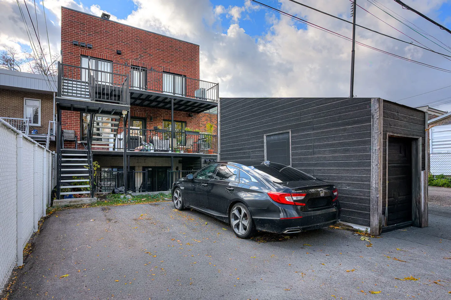 Backyard view of a brick apartment building with black balconies and stairs, a black car, and a black garage.