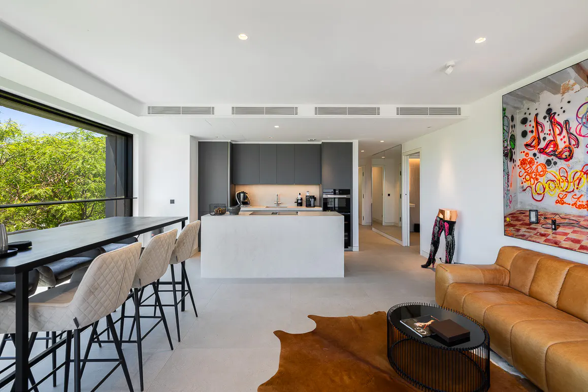 Modern open-plan kitchen and living area with a tan leather sofa, cowhide rug, and large graffiti art on the wall.