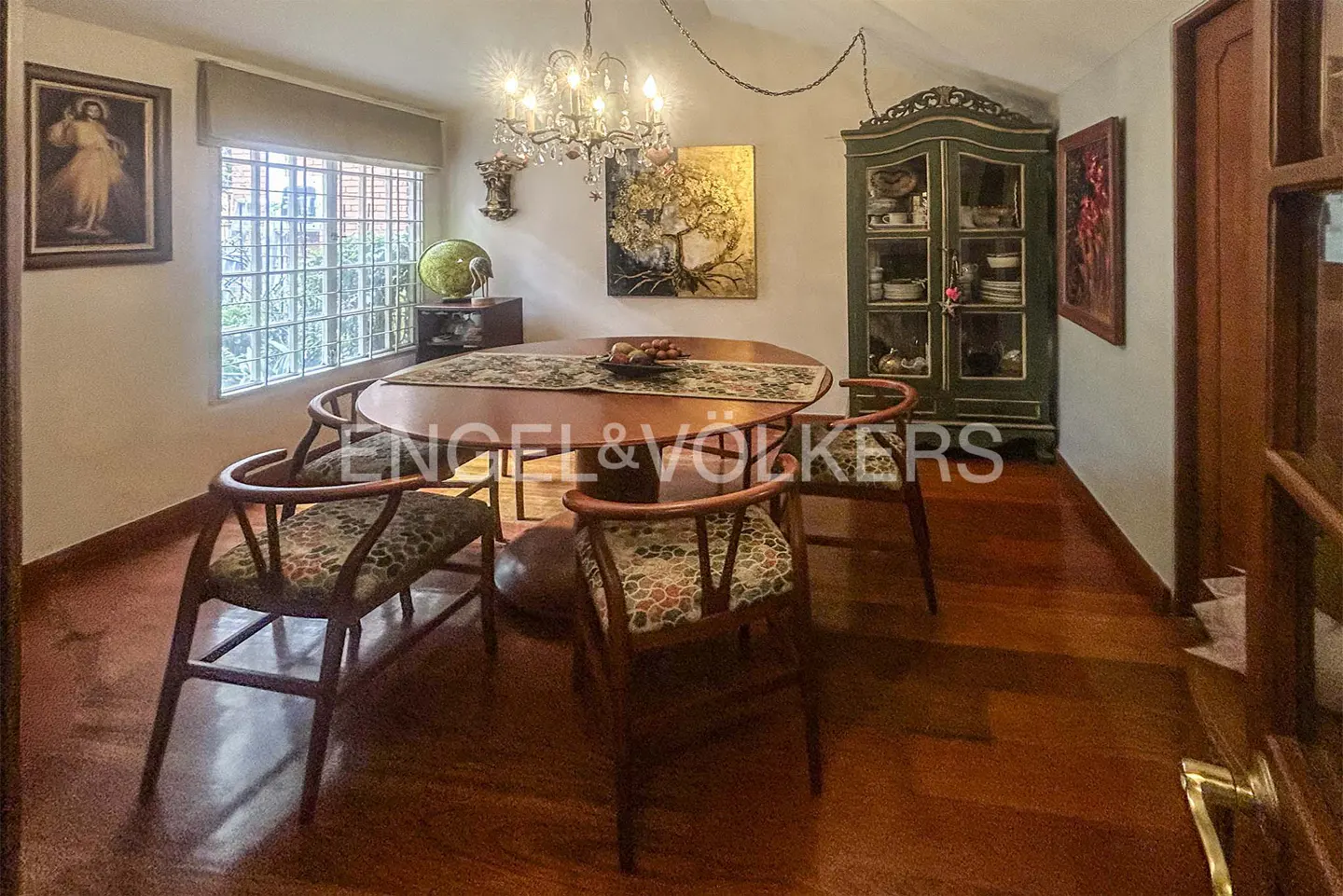 A dining room with a wooden table, chairs, chandelier, and a green cabinet.