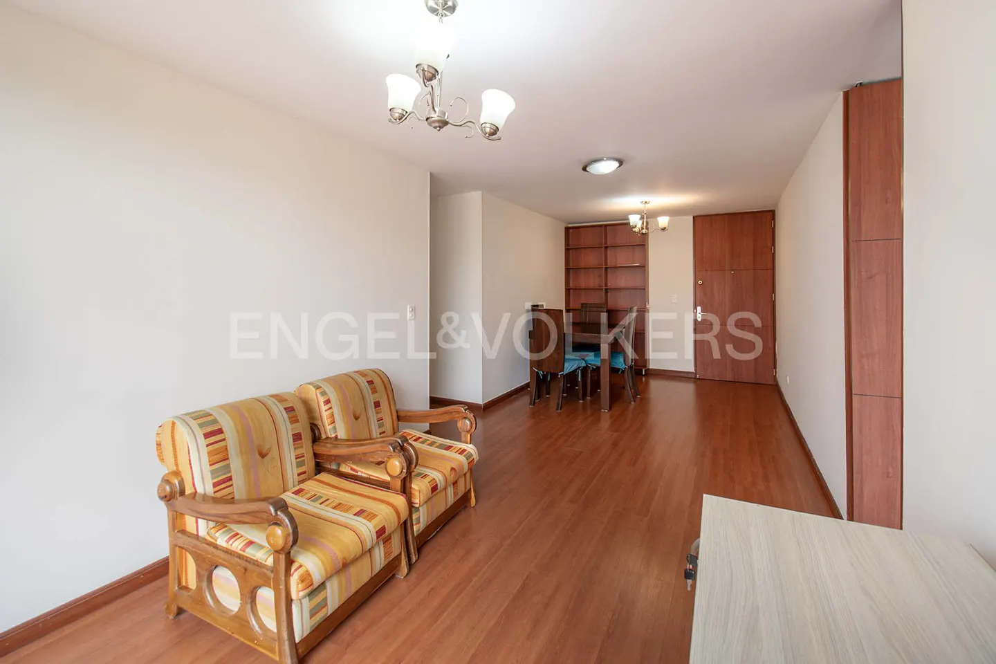 Living room with striped sofa, wood floors, and dining area. Chandelier hangs from the ceiling. Engel & Volkers logo visible.
