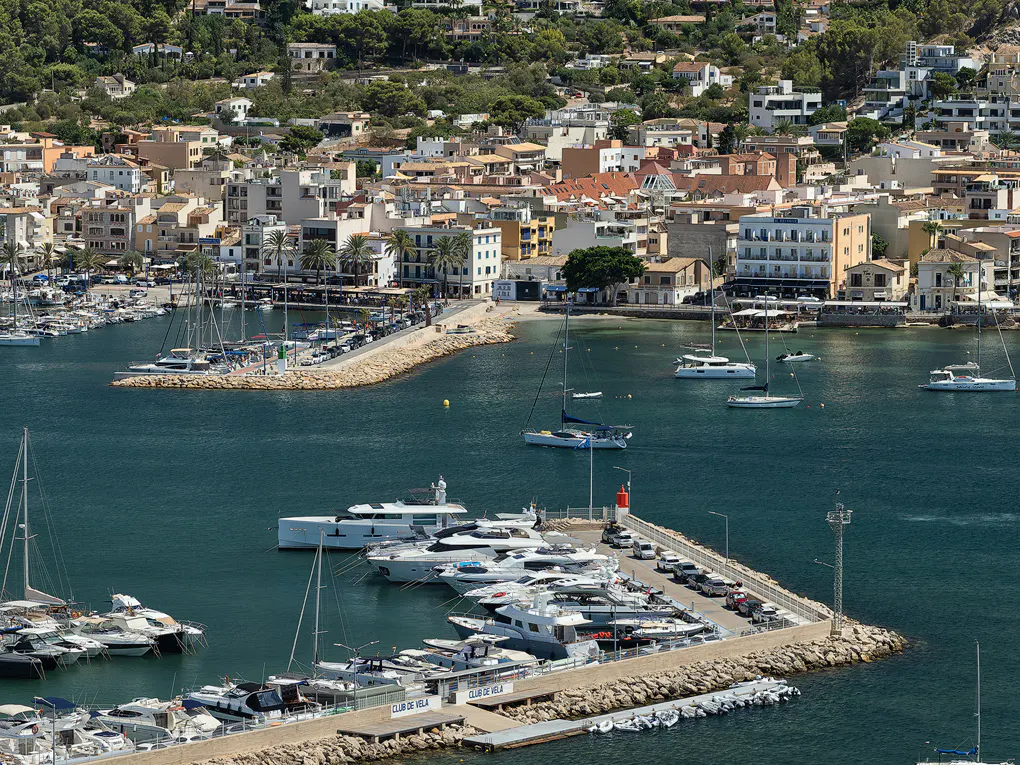 Aerial view of a harbor filled with yachts and boats, a town with white buildings in the background.