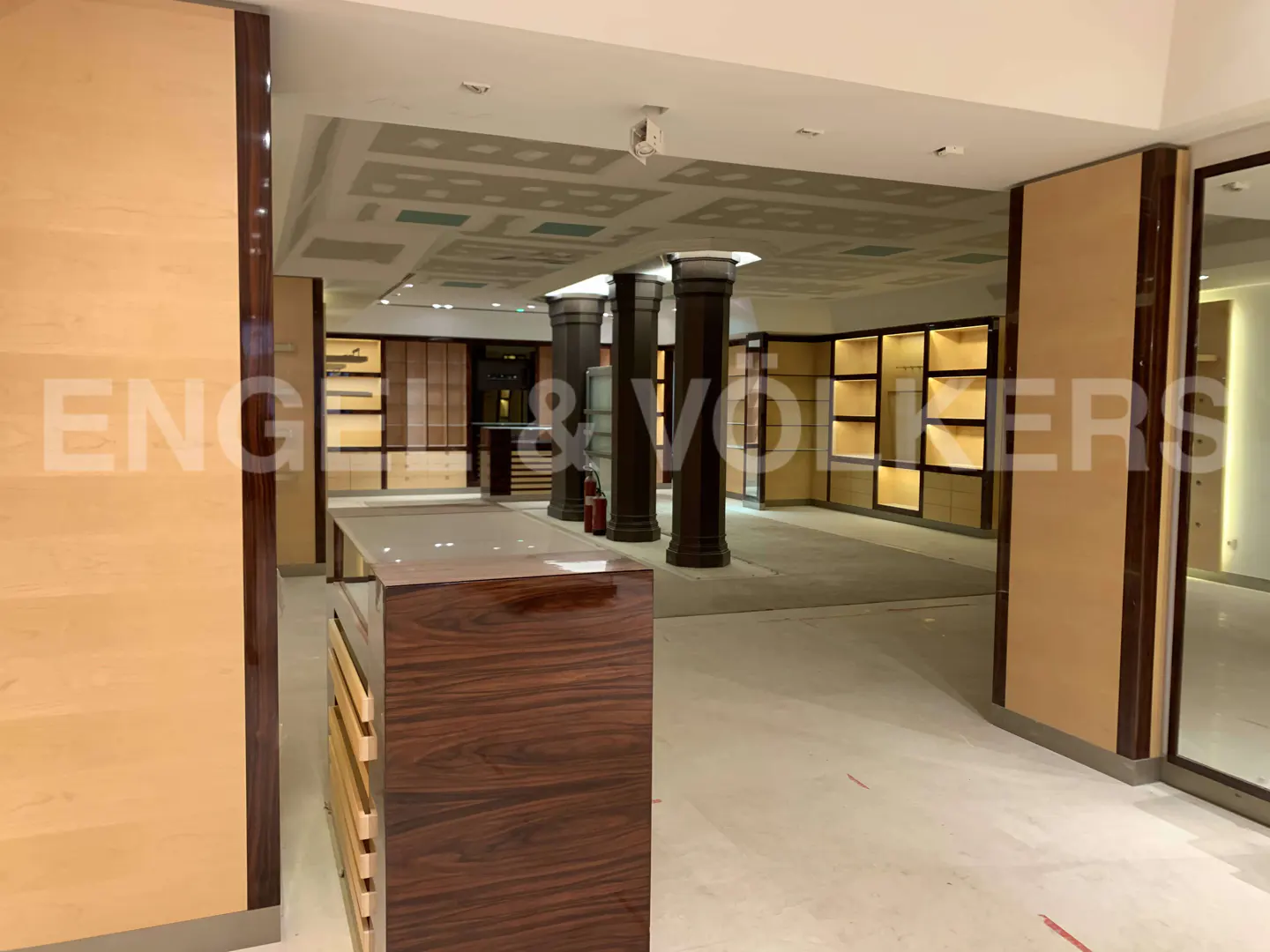 Interior of a retail space under construction with dark wood columns, light wood paneling, and illuminated display shelves.