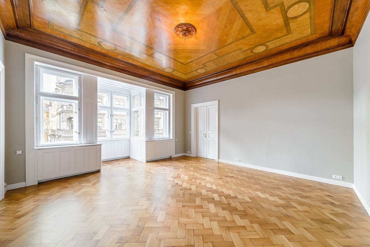 Empty room with herringbone wood floors, light gray walls, white trim, and a decorative, glossy wood-paneled ceiling. [AI-generated text]