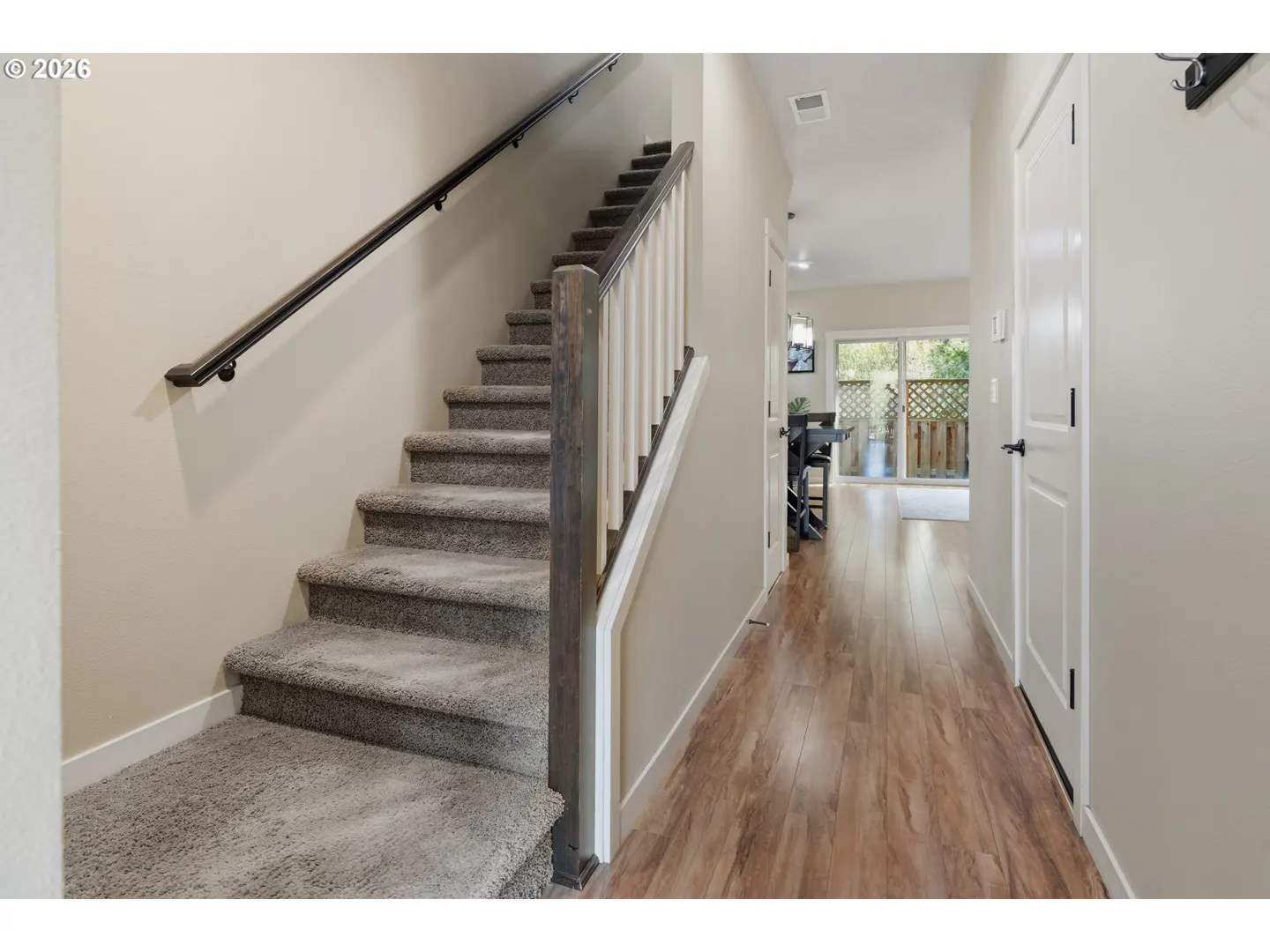 Interior view of a home featuring carpeted stairs with a dark handrail, a hallway with wood floors, and a white door.
