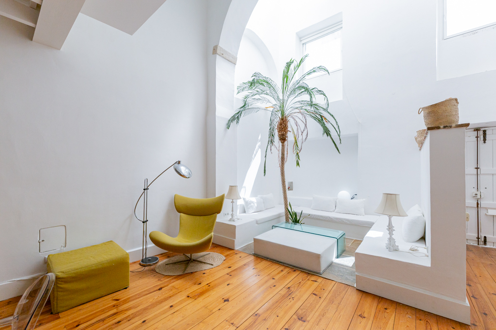 Bright living room with high arched ceilings, white built-in seating, a yellow armchair, and a tall indoor palm tree.