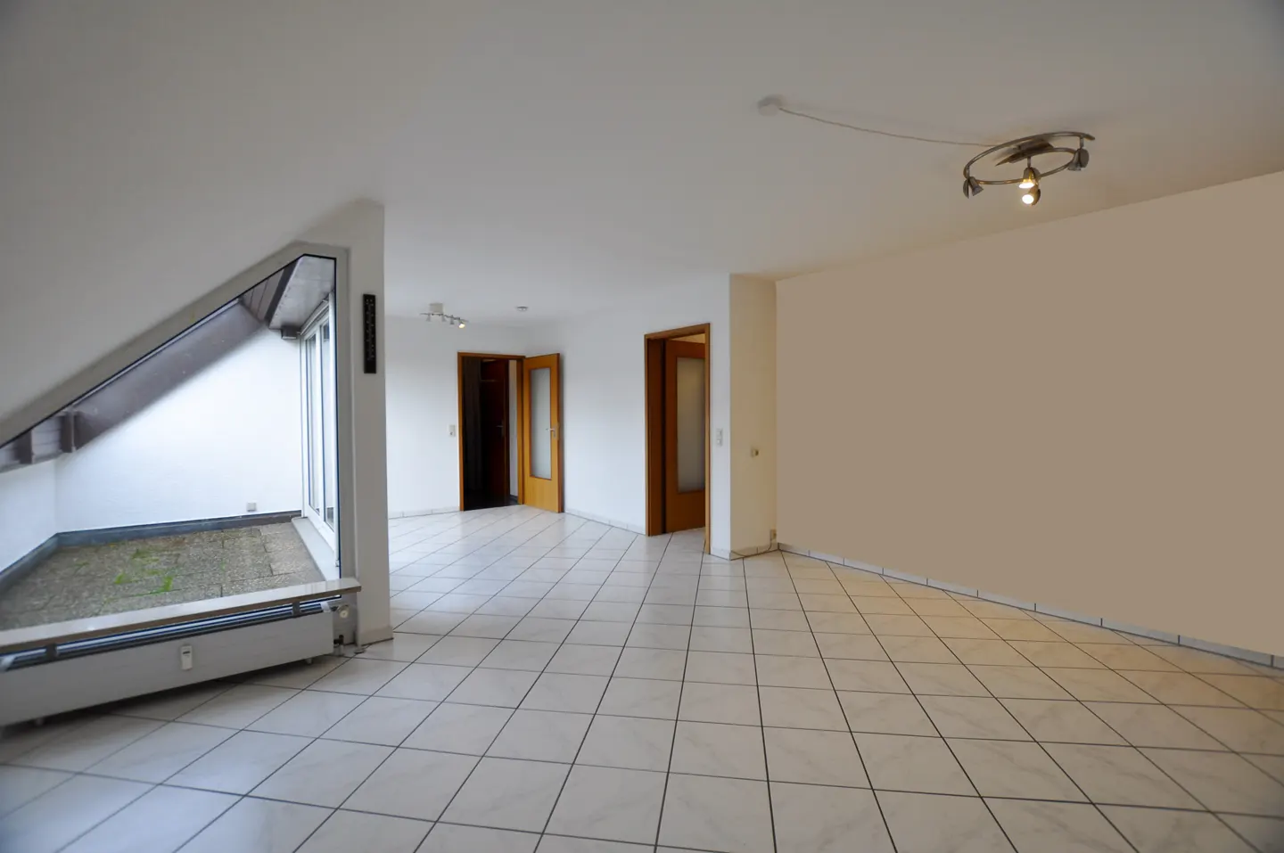 Bright, empty room with white tile floor, white walls, and two open wood doors. A small indoor patio is visible on the left.