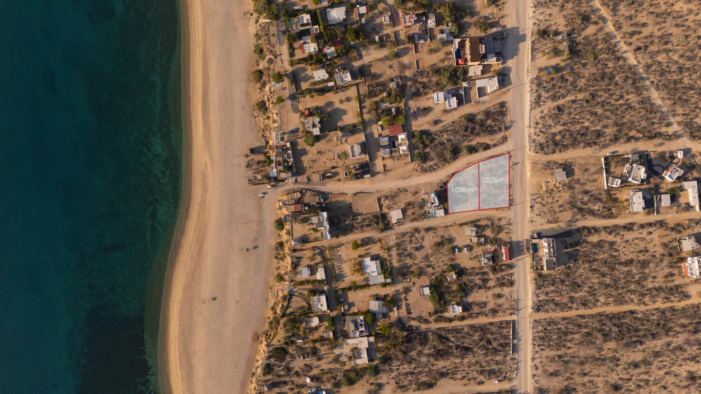 Aerial view of two adjacent vacant lots outlined in red, 1,018m² and 1,026m², near a sandy beach and turquoise ocean.