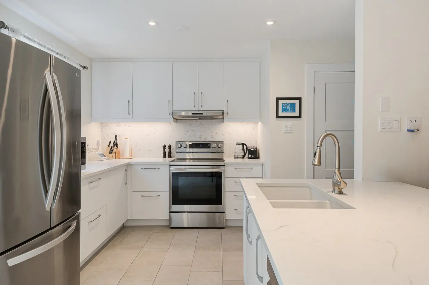Bright, modern kitchen with white cabinets, stainless steel appliances, and a marble countertop island with a sink.