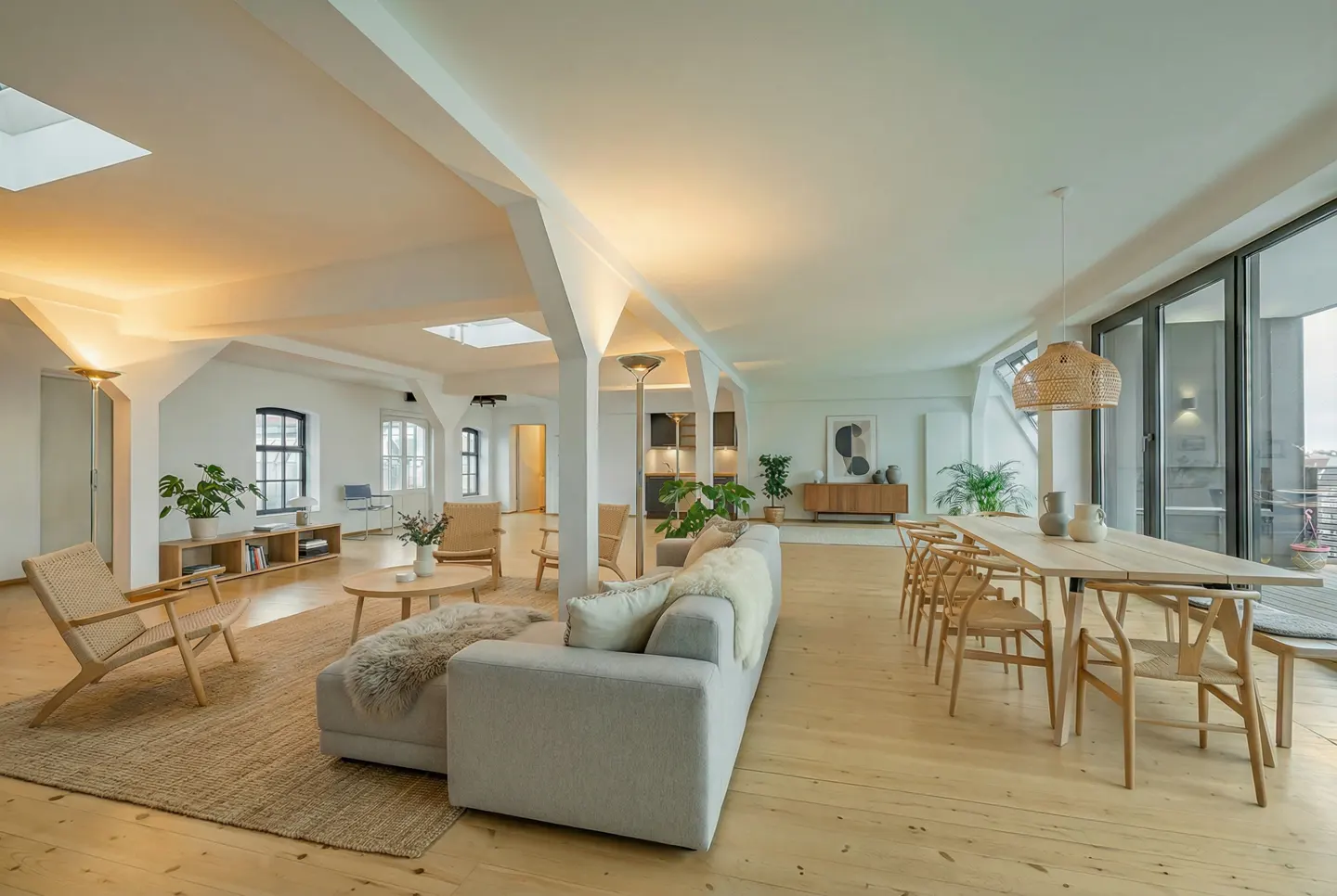 Spacious open-plan living area with light wood floors, a grey sofa, dining table, and modern minimalist decor.