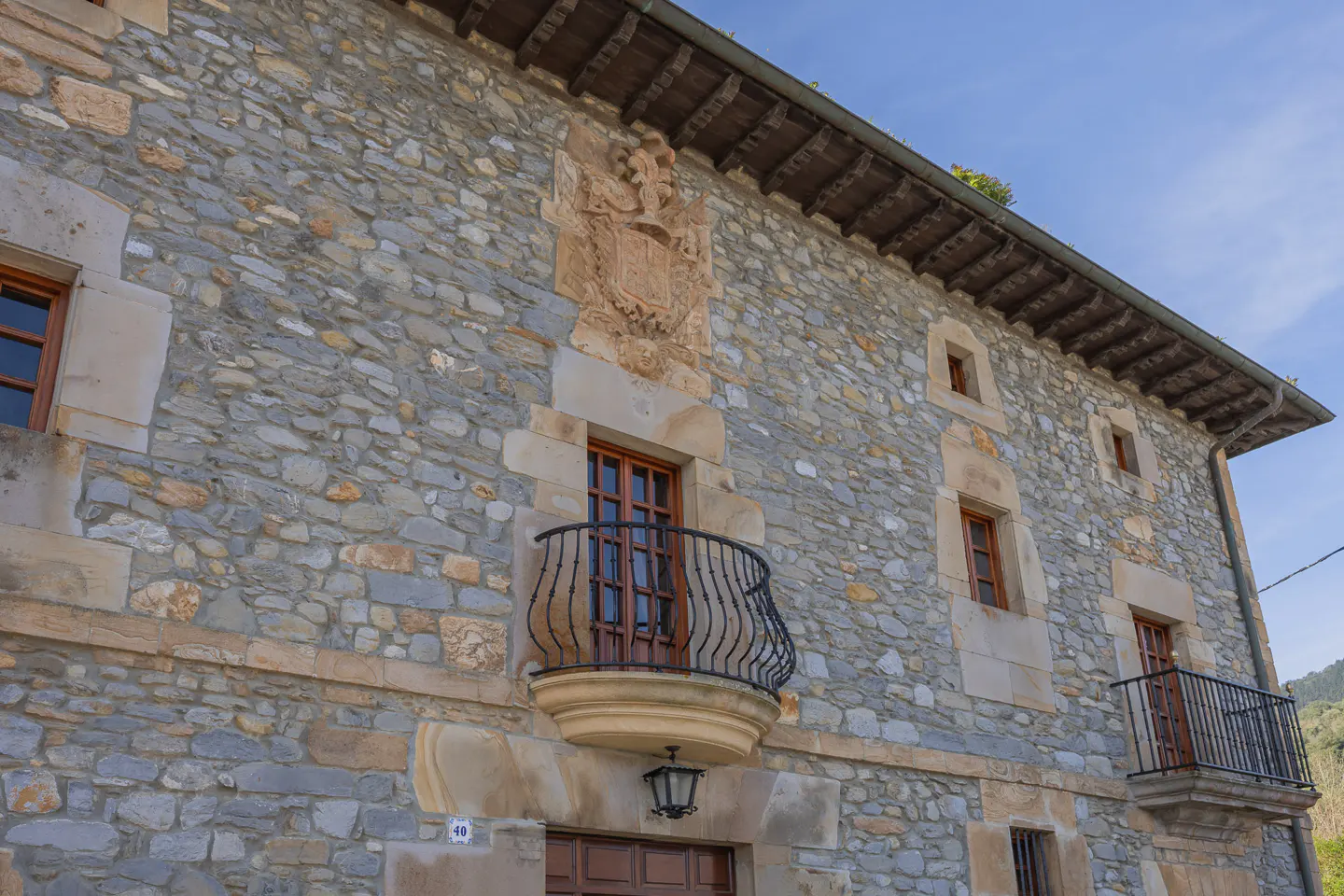 Exterior view of a stone house with wooden windows and wrought iron balconies. A coat of arms is above the first balcony.