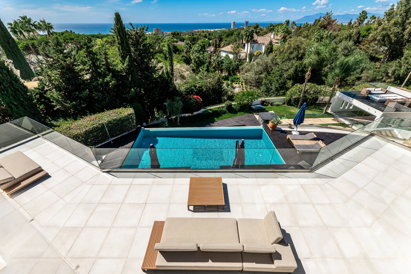 Aerial view of a luxury villa patio with a pool, lounge furniture, and ocean views.