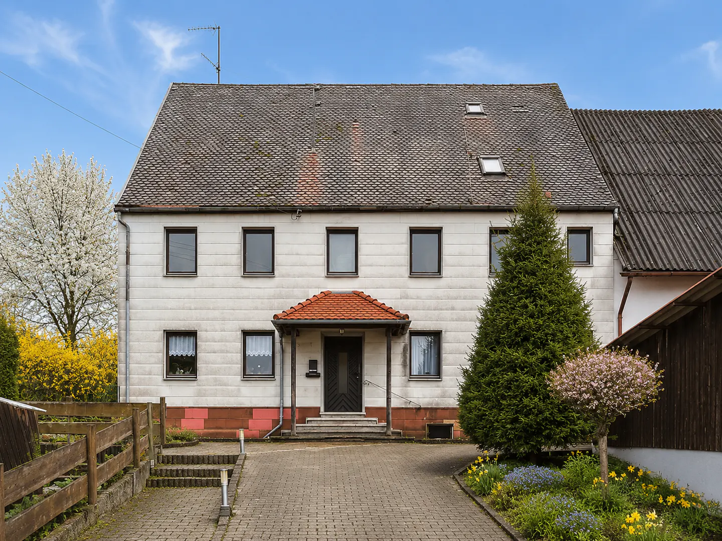 Two-story house with a gray tiled roof, white siding, and a brick walkway leading to the front door.