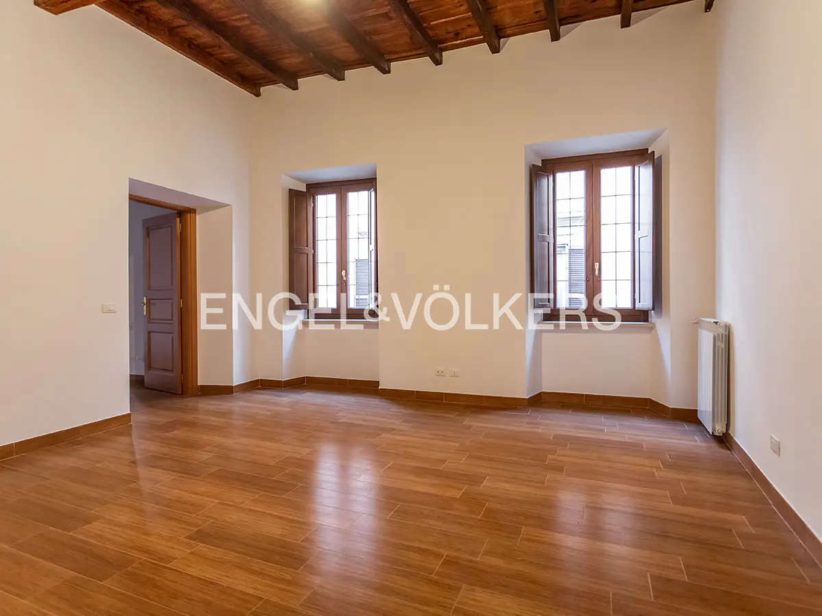 Empty room with wood floors, white walls, and a wood ceiling. Two windows with brown shutters let in light. Doorway on the left.
