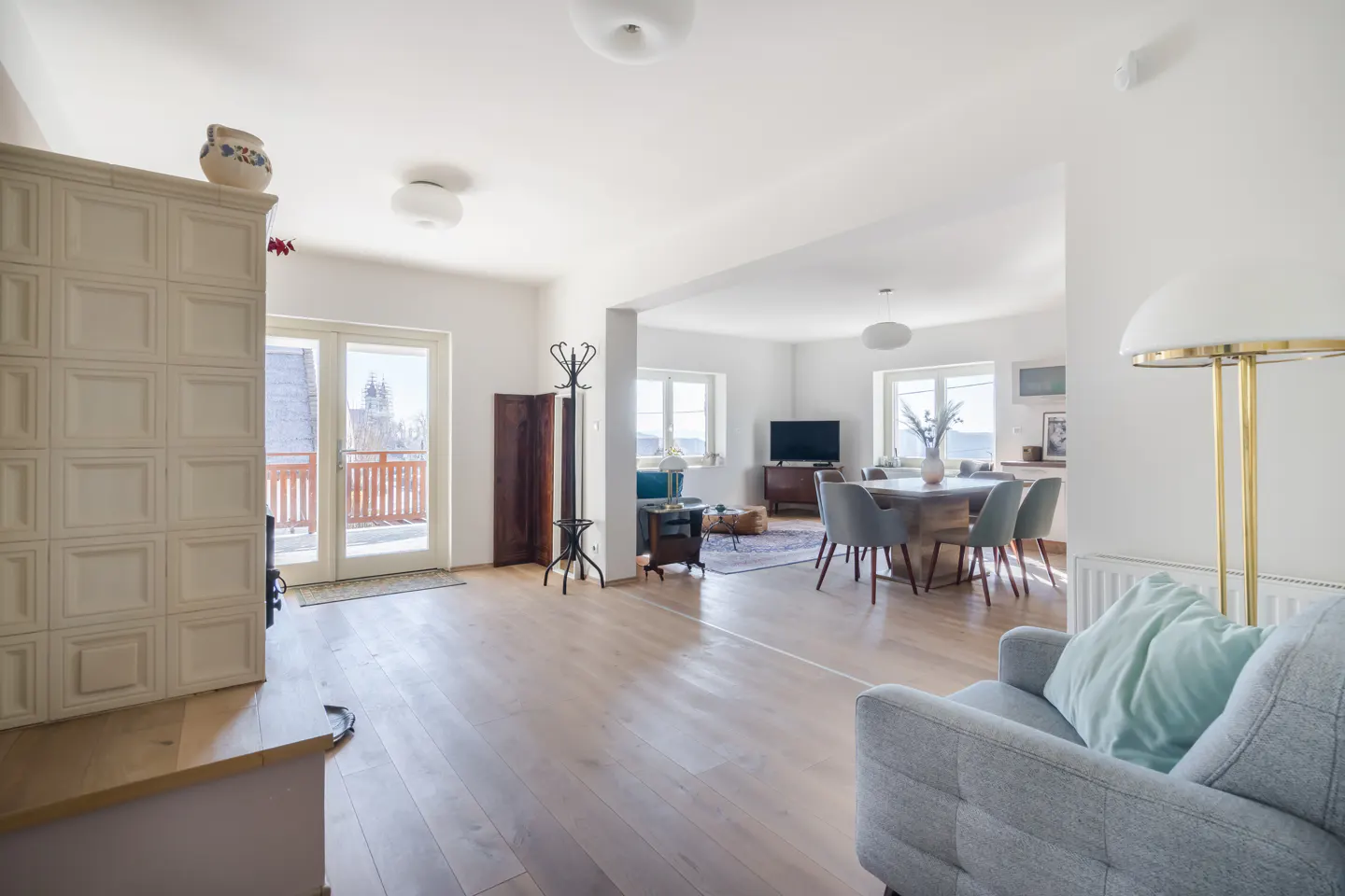 Bright, open-concept living and dining area with light wood floors, white walls, and a tiled fireplace. A gray sofa and dining set add modern touches.