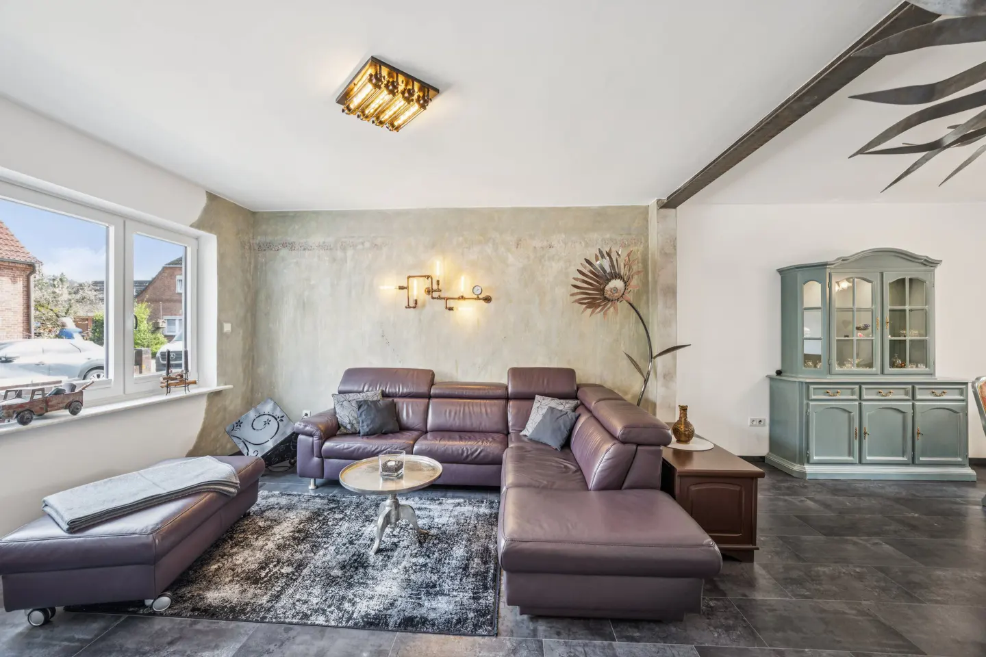 Living room with a purple leather sectional sofa, a gray rug, and a blue cabinet. A window is on the left.