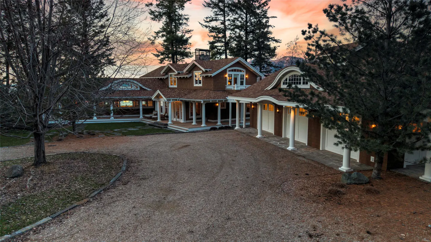 A brown house with white pillars and a gravel driveway at dusk.