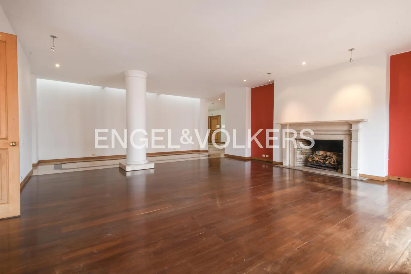 Spacious living room with hardwood floors, white walls, and a fireplace. A white column stands near the Engel & Völkers logo.