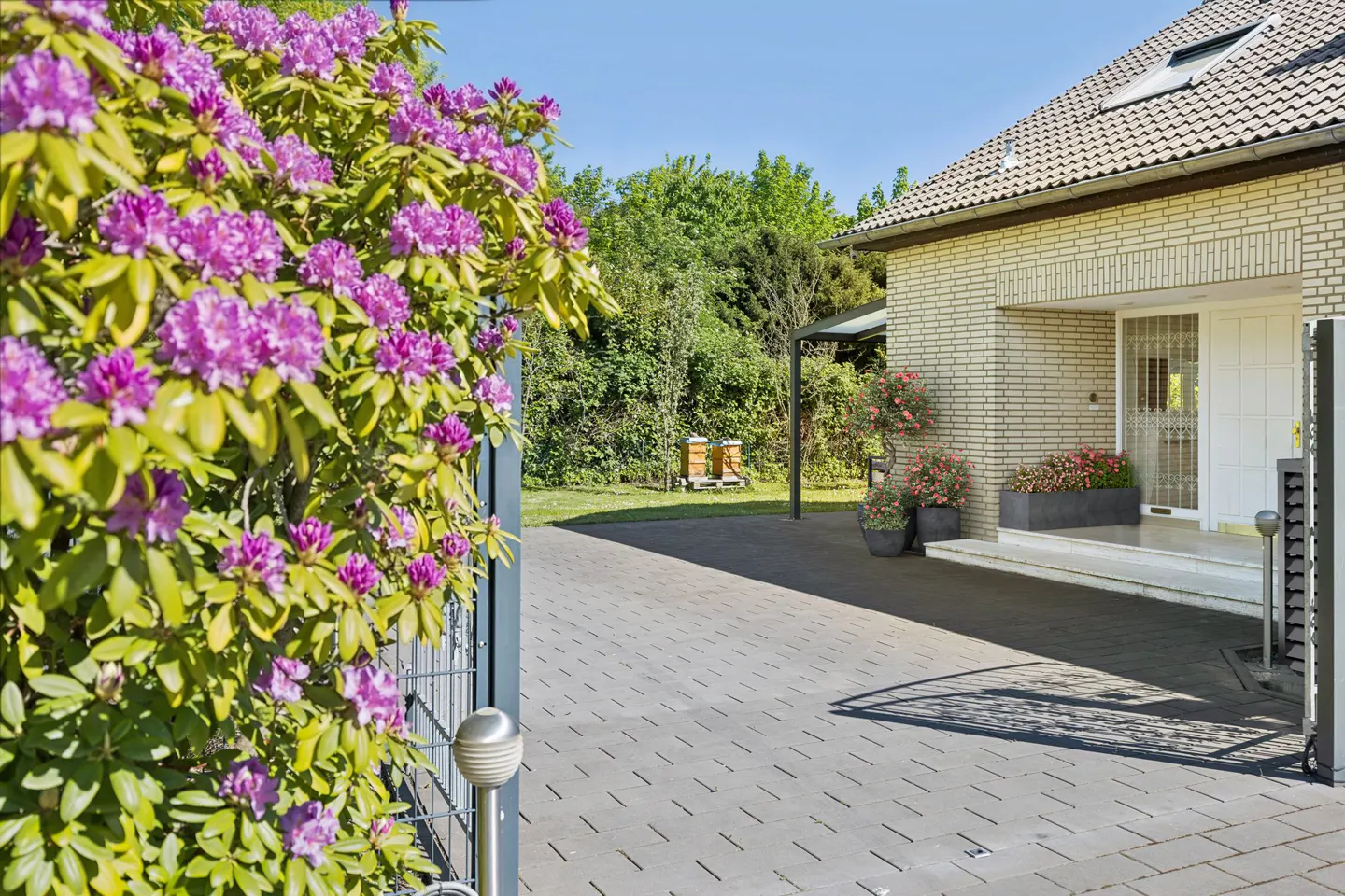 Exterior view of a brick house with a gray tiled roof, a paved driveway, and purple flowers in the foreground.