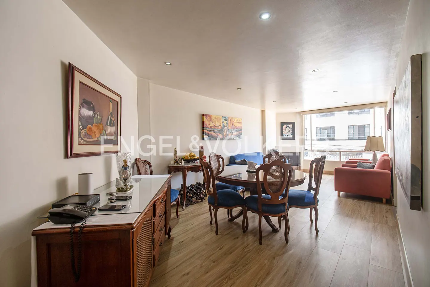 Bright, open-concept living and dining area with wood floors, blue chairs, and a large window. Artwork adorns the walls.