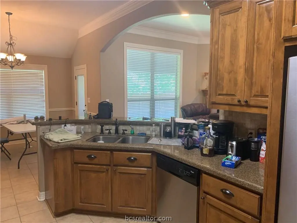 Kitchen with wood cabinets, granite countertops, double sink, and dishwasher, opening into a dining area with a chandelier.