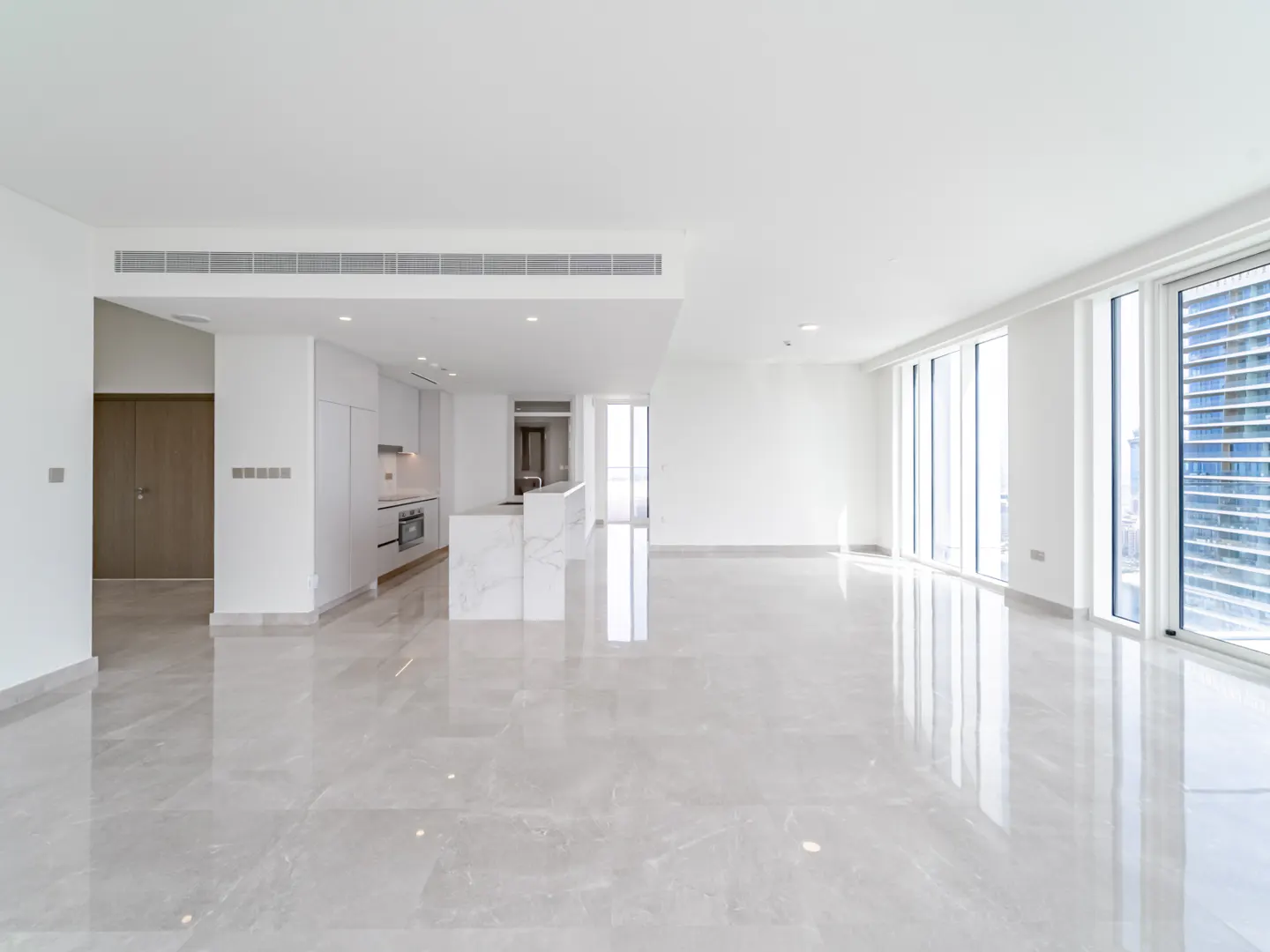 Modern, minimalist open-plan living area with white walls, marble floors, and a sleek kitchen with a marble island.