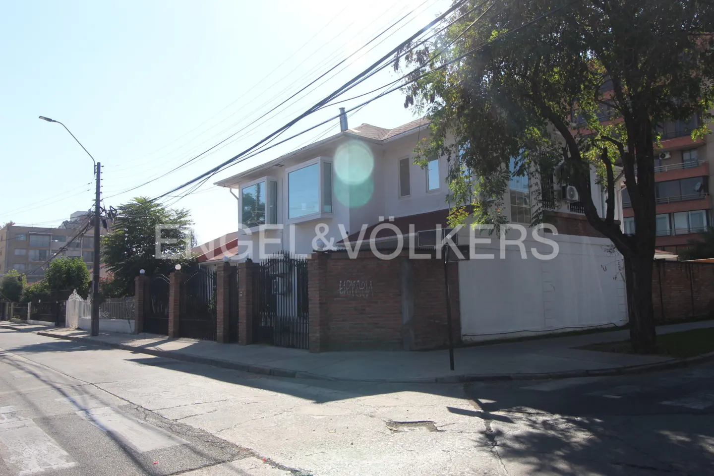 Exterior view of a two-story house with white walls, large windows, and a brick fence, street view.