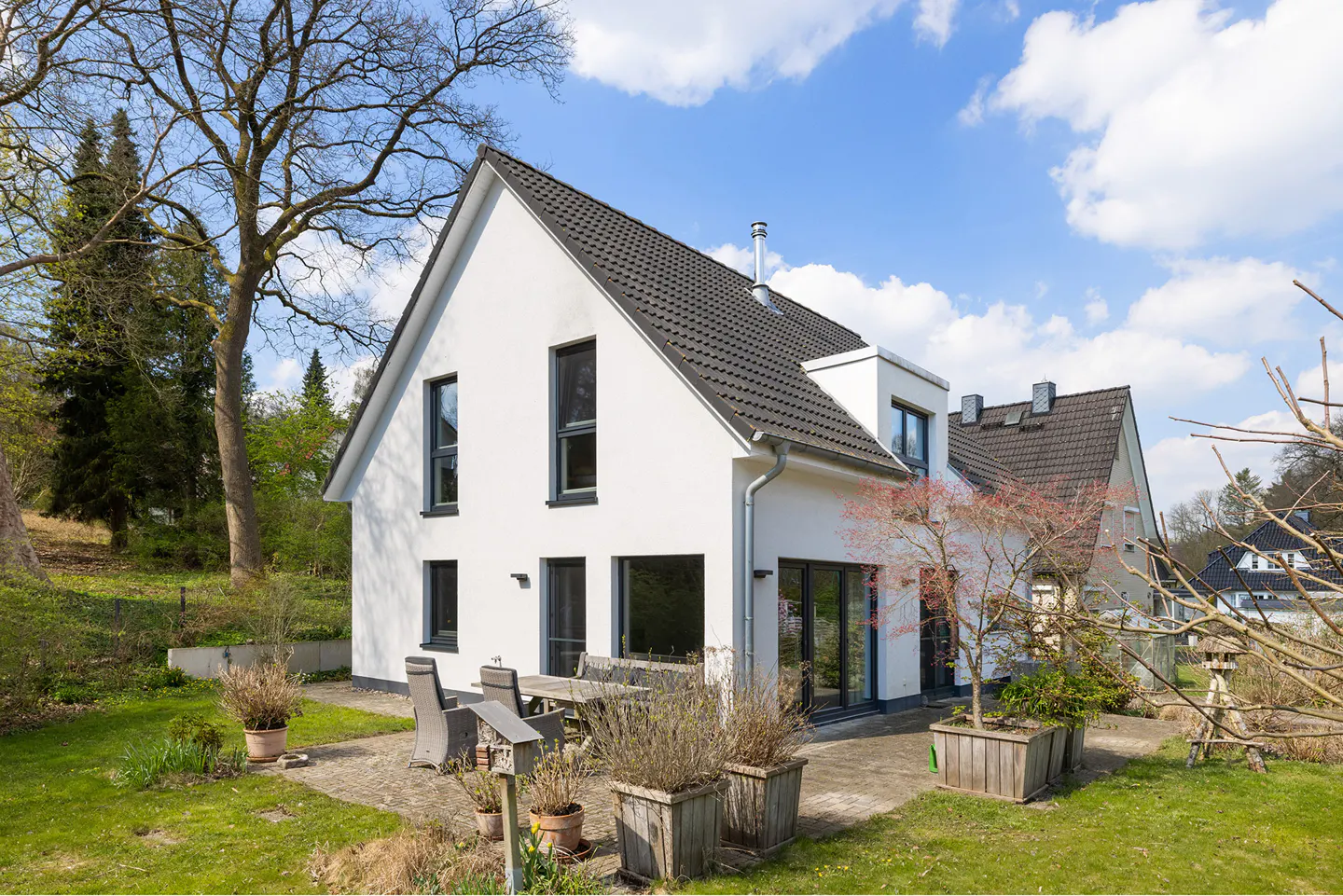 Modern white house with a dark gray roof, black framed windows, and a patio with a wooden table and chairs.
