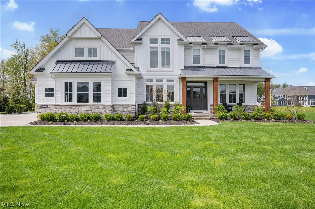 Two-story white farmhouse with gray roof and stone accents, set on a green lawn under a blue sky.