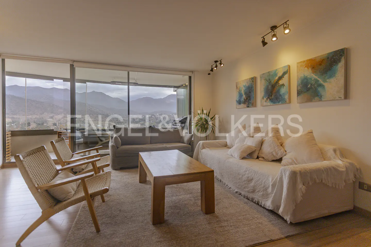 Living room with two sofas, wooden chairs, and a coffee table. Large windows offer mountain views. Abstract art hangs on the wall.