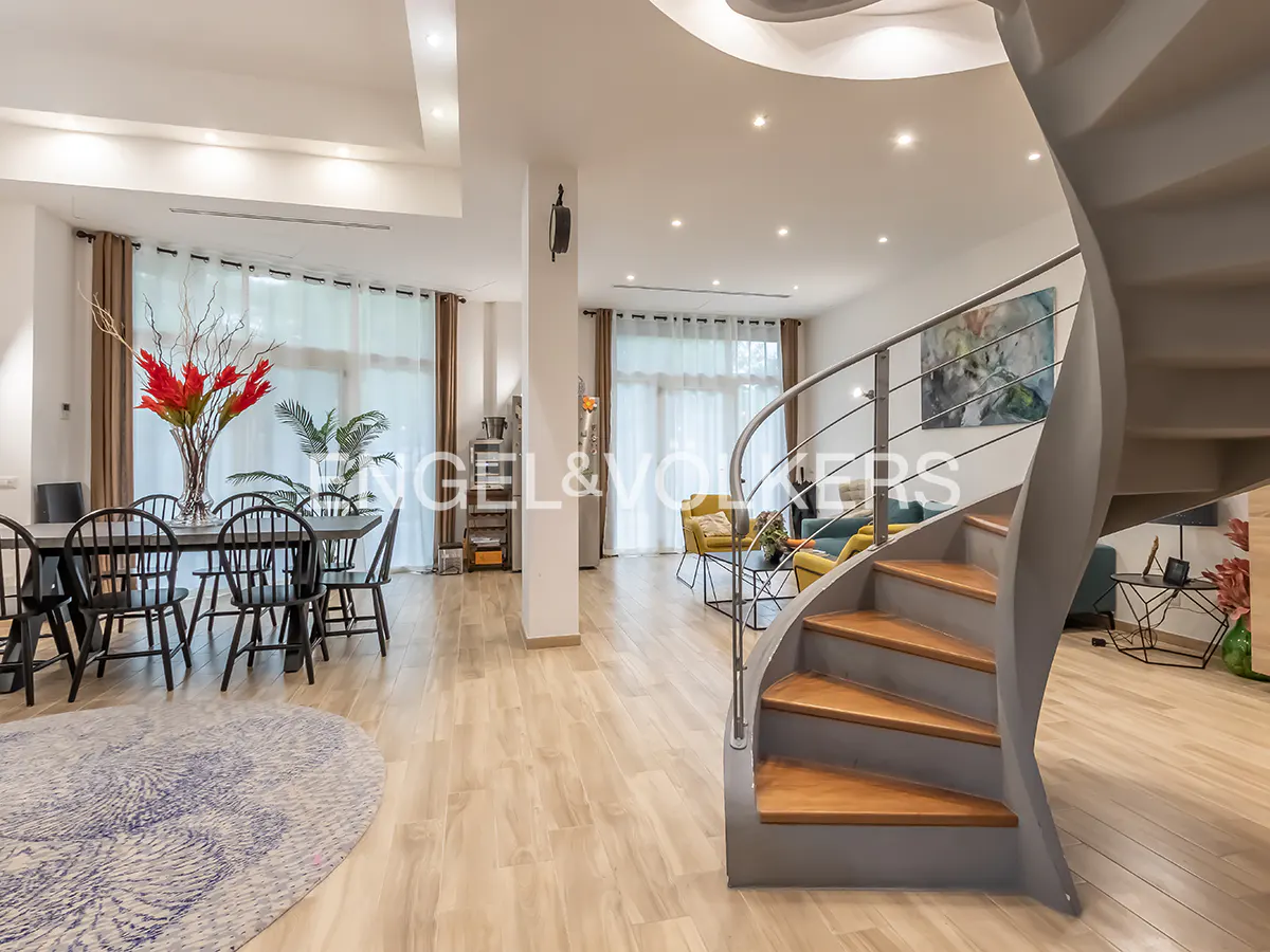 Bright, open-plan home interior with a spiral staircase, dining table, and living area. Wood floors and large windows.