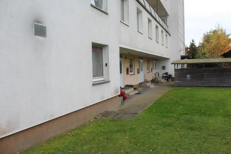 Exterior view of a white apartment building with a green lawn. Windows and doors are visible.