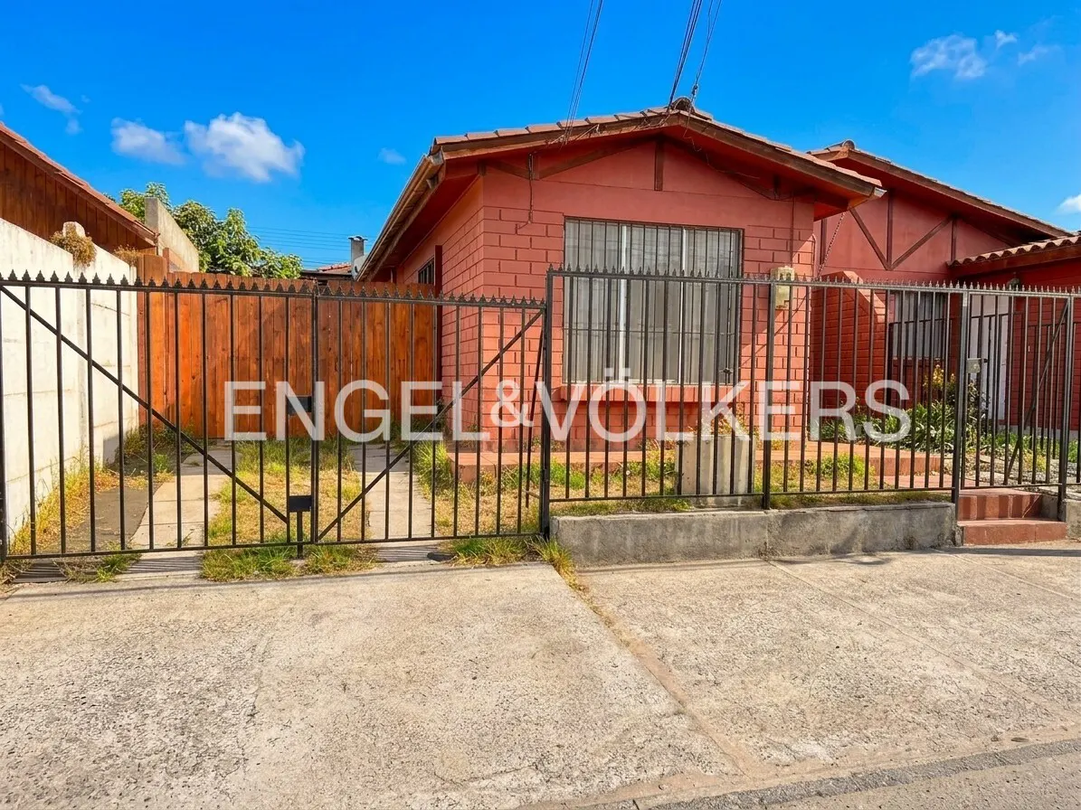 A red brick house with a black iron gate and a wooden fence under a blue sky.