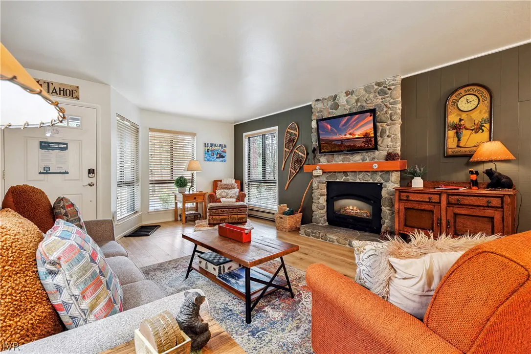 Living room with stone fireplace, TV, wood furniture, and snowshoes on the wall. Sofas are gray and orange. A "Tahoe" sign hangs near the door.