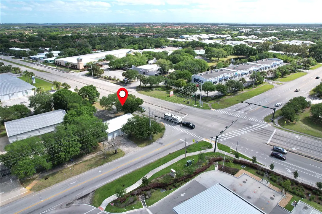 Aerial view of a property with a red location pin, near a road intersection with cars and green trees.