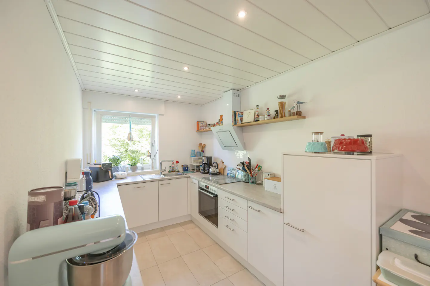 Bright kitchen with white cabinets, light tile floor, and a window. A light blue stand mixer sits on the counter.