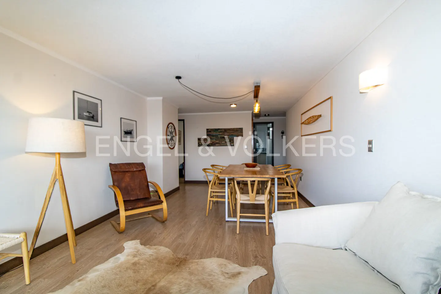 Bright living room with wood floors, white walls, a dining table, a brown leather chair, and a white sofa.