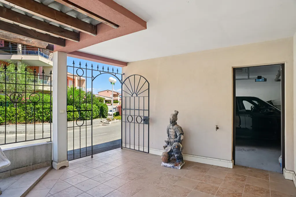 Covered patio with iron gates, a tan tile floor, and a statue of a warrior. A garage with a car is visible through a doorway.
