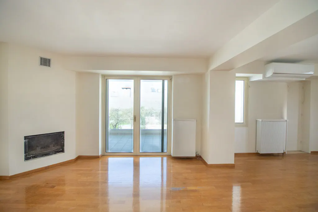 Empty living room with hardwood floors, white walls, fireplace, and sliding glass doors to a balcony.
