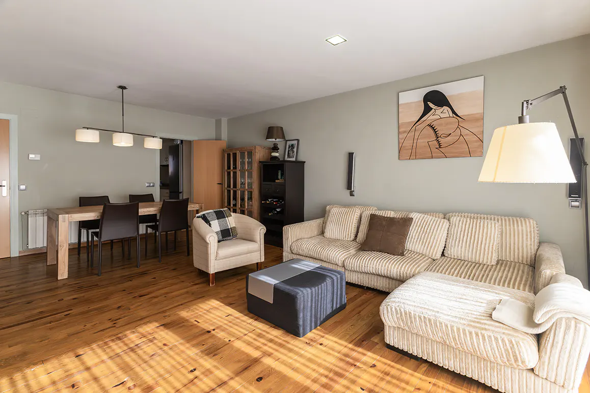 Living room with a beige corduroy sofa, armchair, and ottoman on a wood floor. A dining table and chairs are in the background.