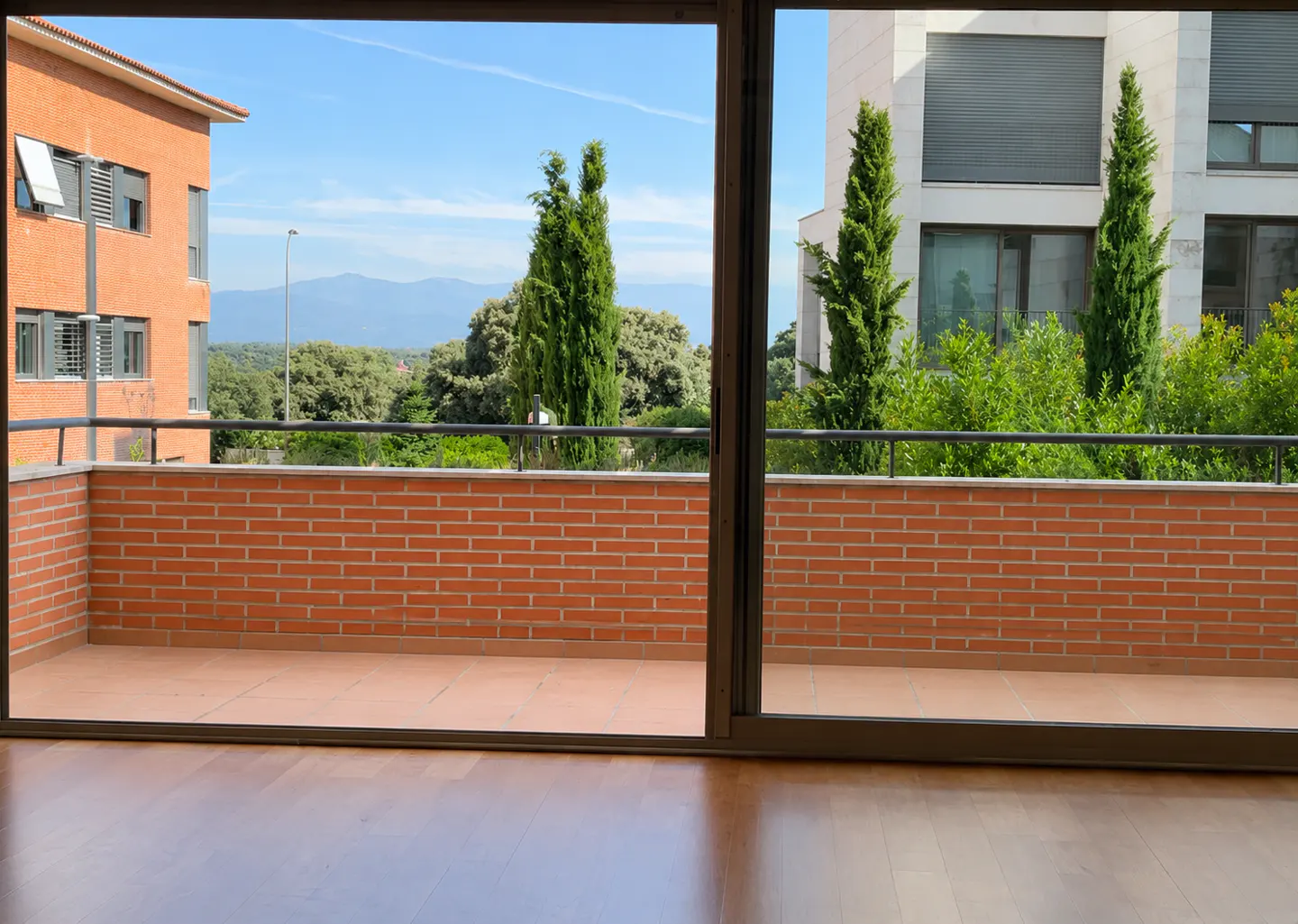 View from inside looking out onto a brick balcony with a view of trees, nearby buildings, and distant mountains.