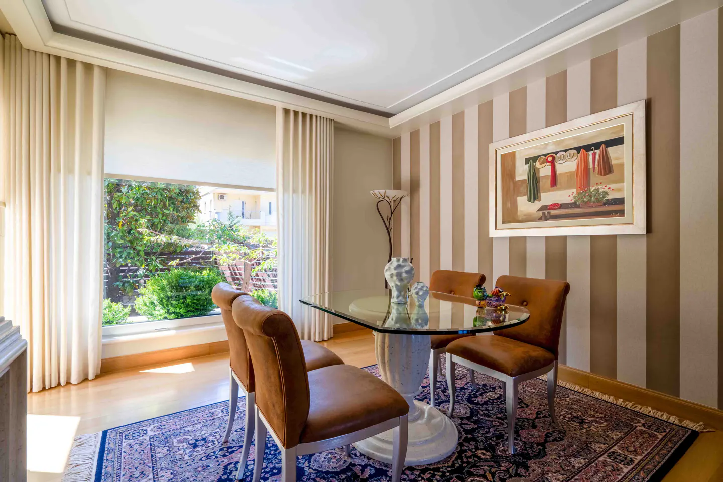 Dining room with glass table, brown leather chairs, and striped wallpaper. A window shows a lush green garden.